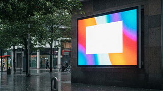 Ein großer LED-Outdoor-Bildschirm im Regenwetter Auf einem großen Platz in einer Großstadt steht ein riesiger LED-Display, der den Platz beleuchtet. Das Bild ist in Blau und Dunkel gehalten. Durch das regnerische Wetter reflektieren die Farben auf den Bodenplatten des Platzes.