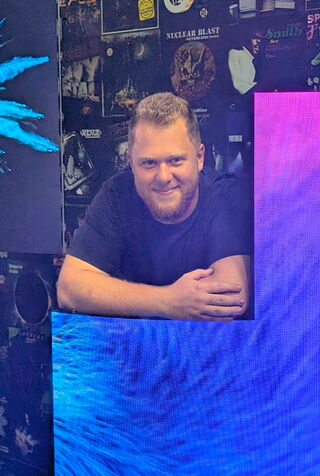 Oliver Vogt Ein junger Mann steht hinter einer LED-Wand die das Logo der Unilumin Germany GmbH zeigt.