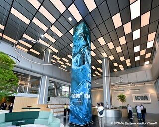 Ein moderner Empfangsbereich einer Firma. Neben des Empfangstresen befinden sich eine Sitzecke im Eingangsbereich. Der Blickfang bildet eine Säule, die mit LED-Wänden an allen 4 Ecken ausgestattet wurde.